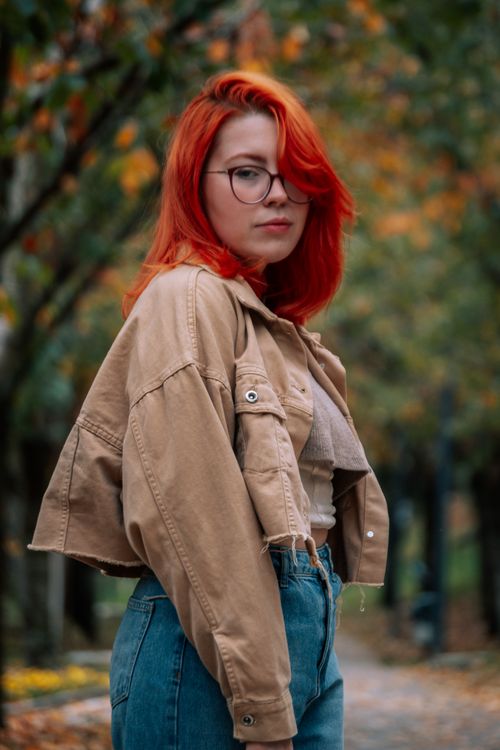 Free Redheaded woman posing outdoors in autumn with fashionable attire and glasses. Stock Photo