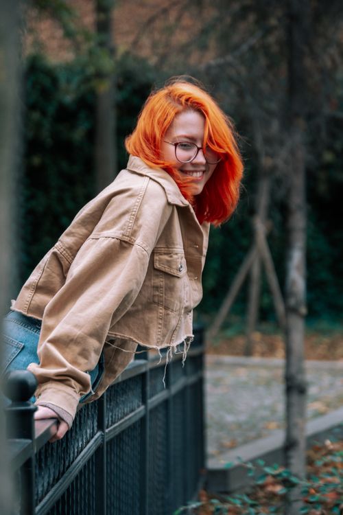 Free A red-haired woman smiling while leaning on a park fence, exuding happiness. Stock Photo