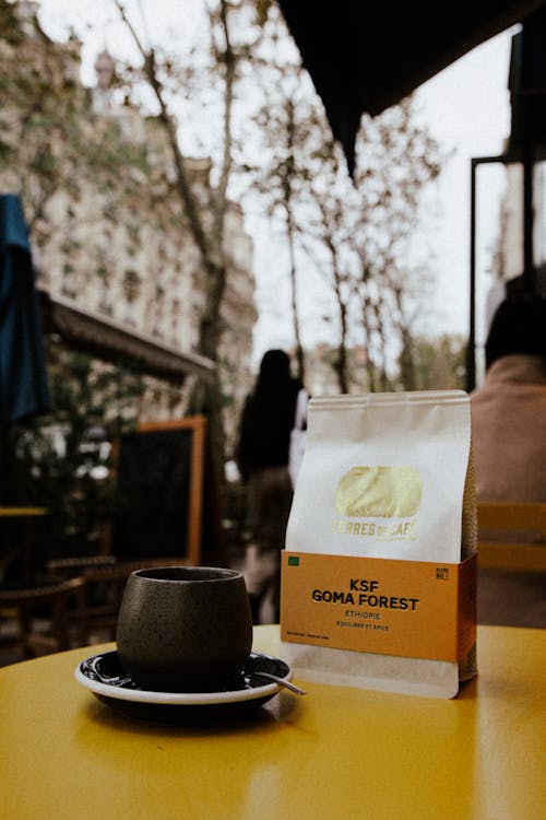 Coffee Cup Next to Paper Bag on Table in Cafe