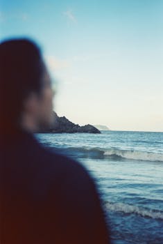 Blurred silhouette at the beach with calm waves and distant hills under a twilight sky.
