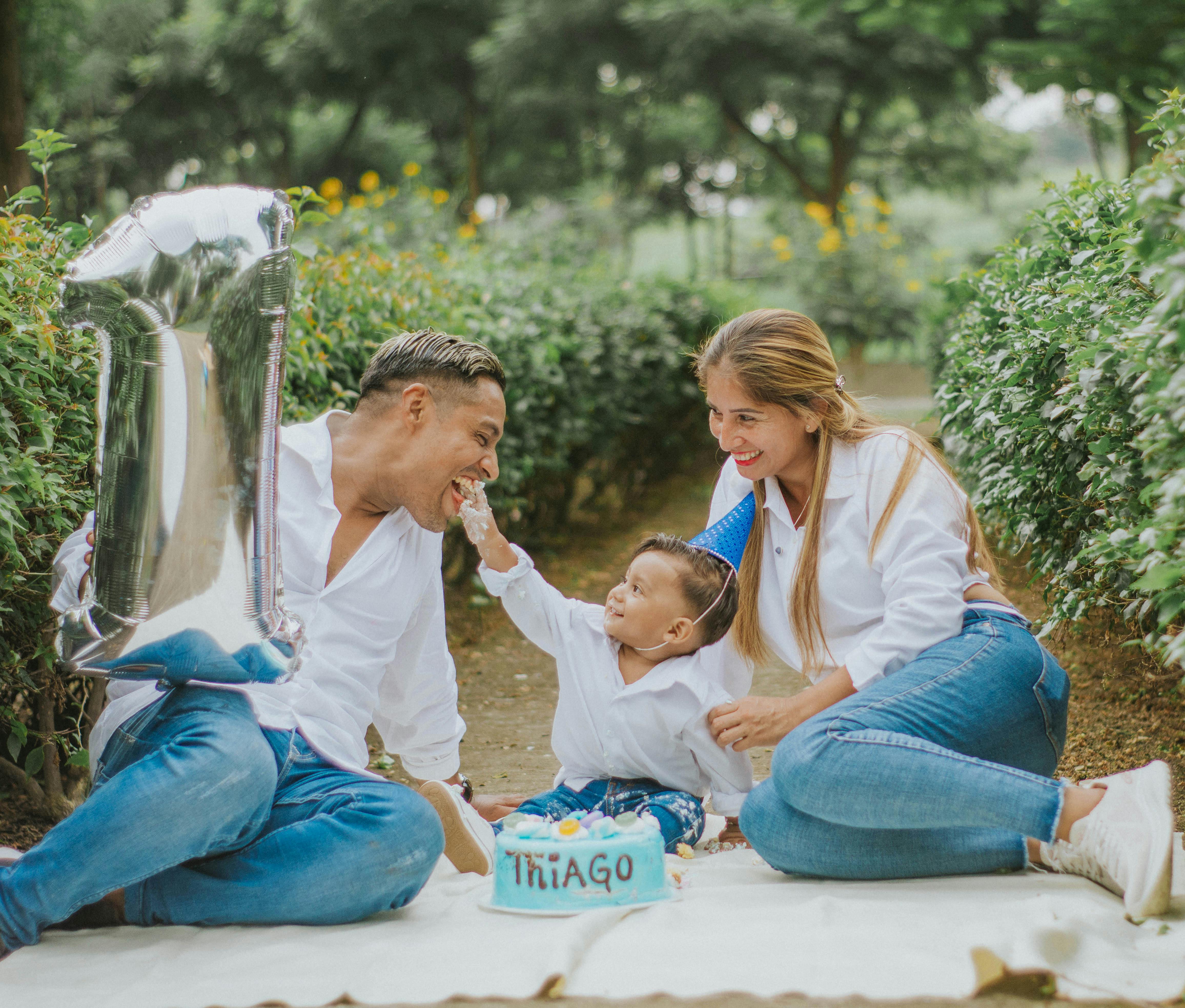 A joyful family celebrating their child's first birthday outdoors with cake and balloons.