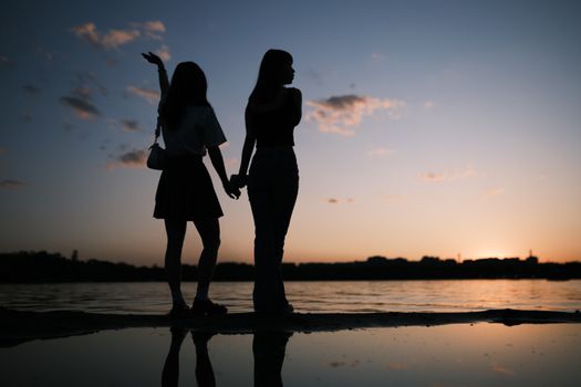 Romantic silhouette of a couple holding hands by the beach at a serene sunset.