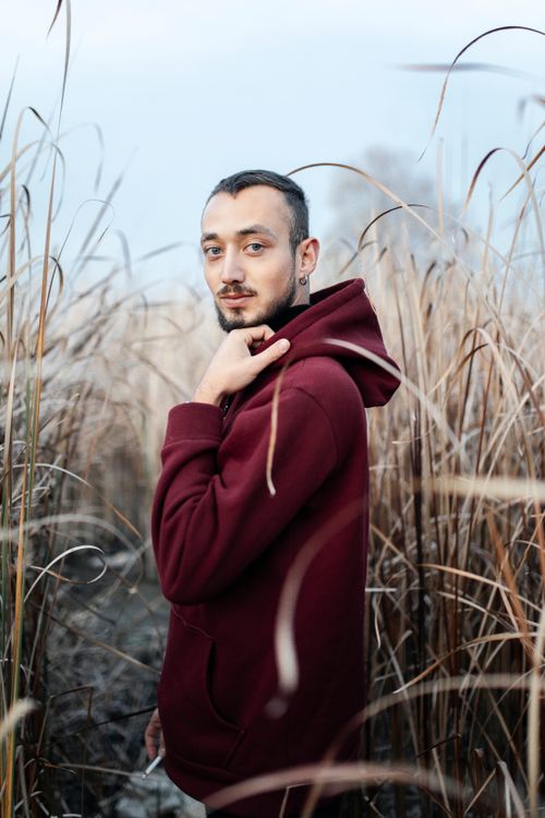 Free Man in a red hoodie posing in a tall grass field during daytime. Stock Photo
