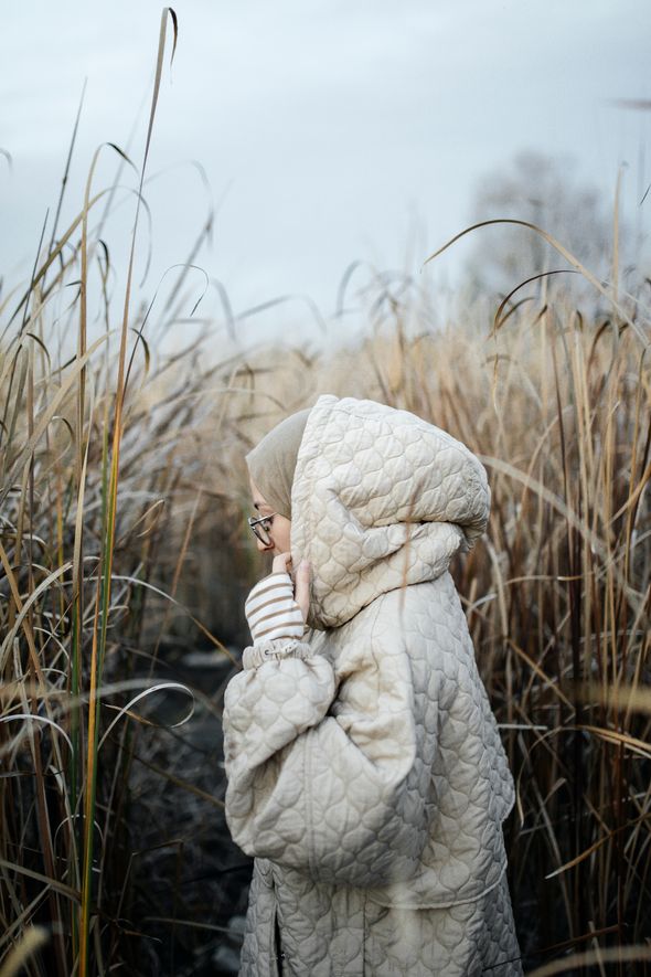 Person in a cream quilted hooded coat in tall winter grass — photo by Esma Atak on Pexels