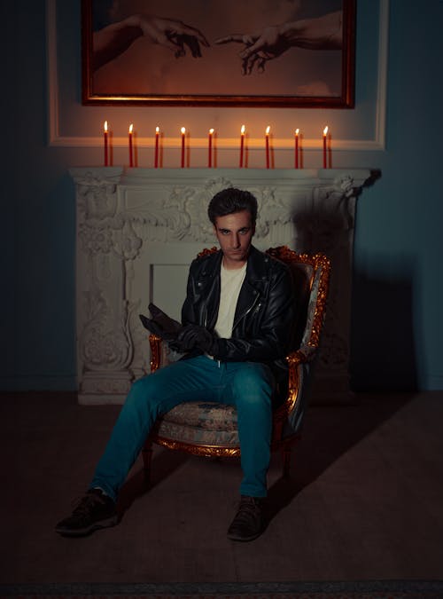 Man in Leather Jacket Sitting on Armchair with Wax Candles behind