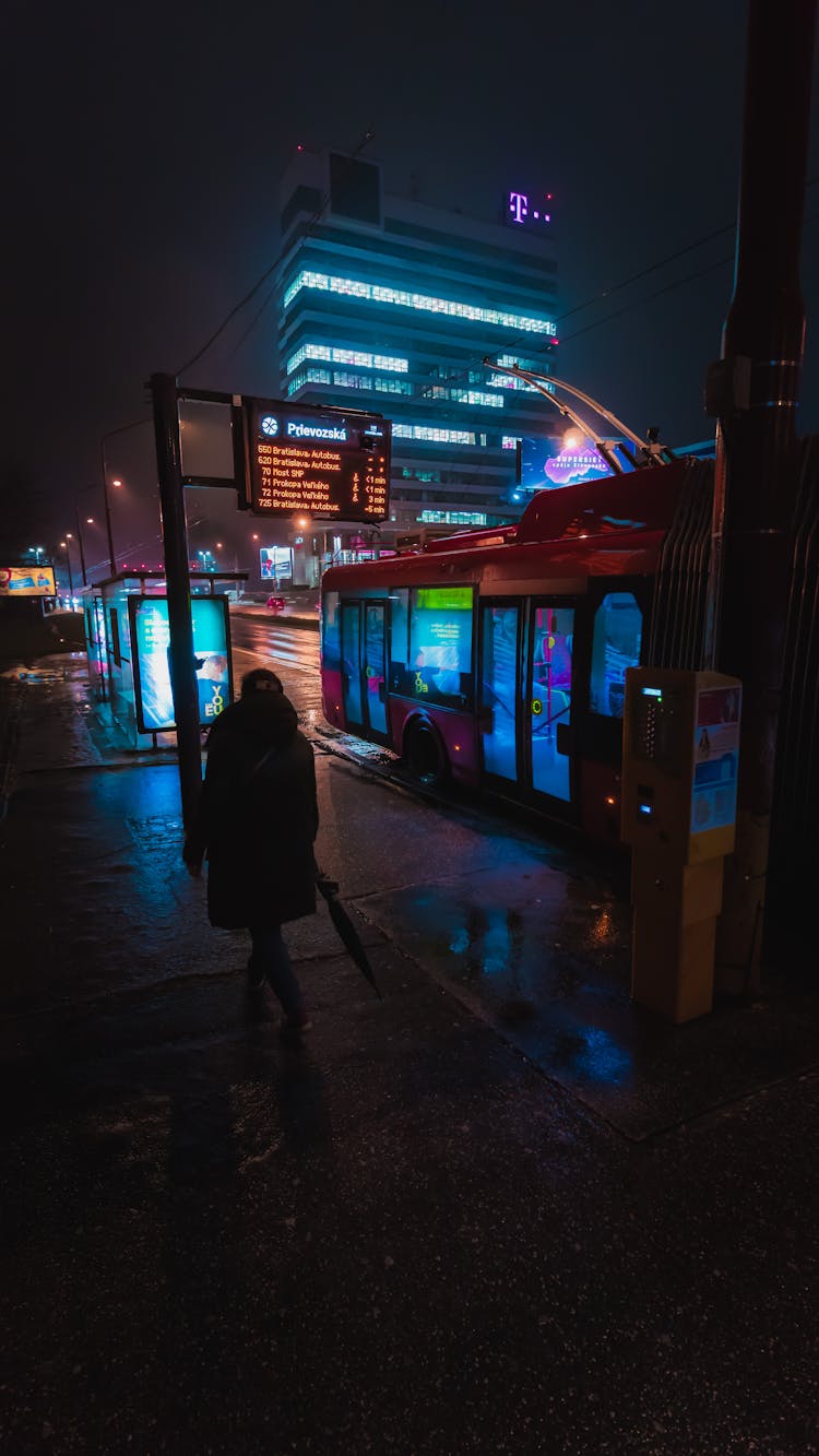 Woman Walking On A Night City Street Past A Trolley Bus Stop, Bratislava, Slovakia