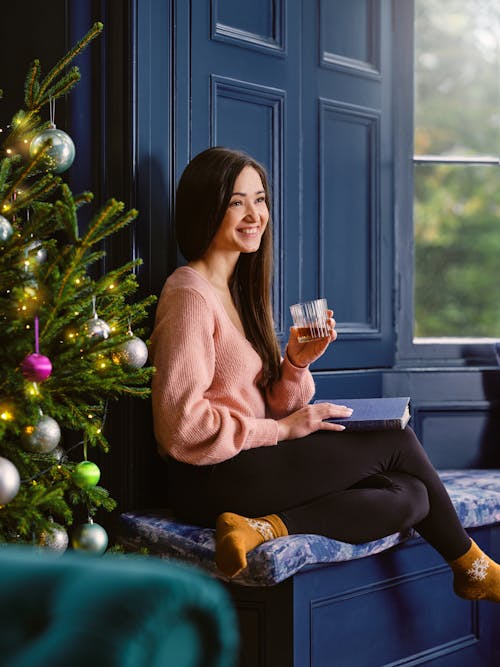 Young Woman Sitting with a Glass of Whiskey on the Blue Furniture by the Christmas Tree