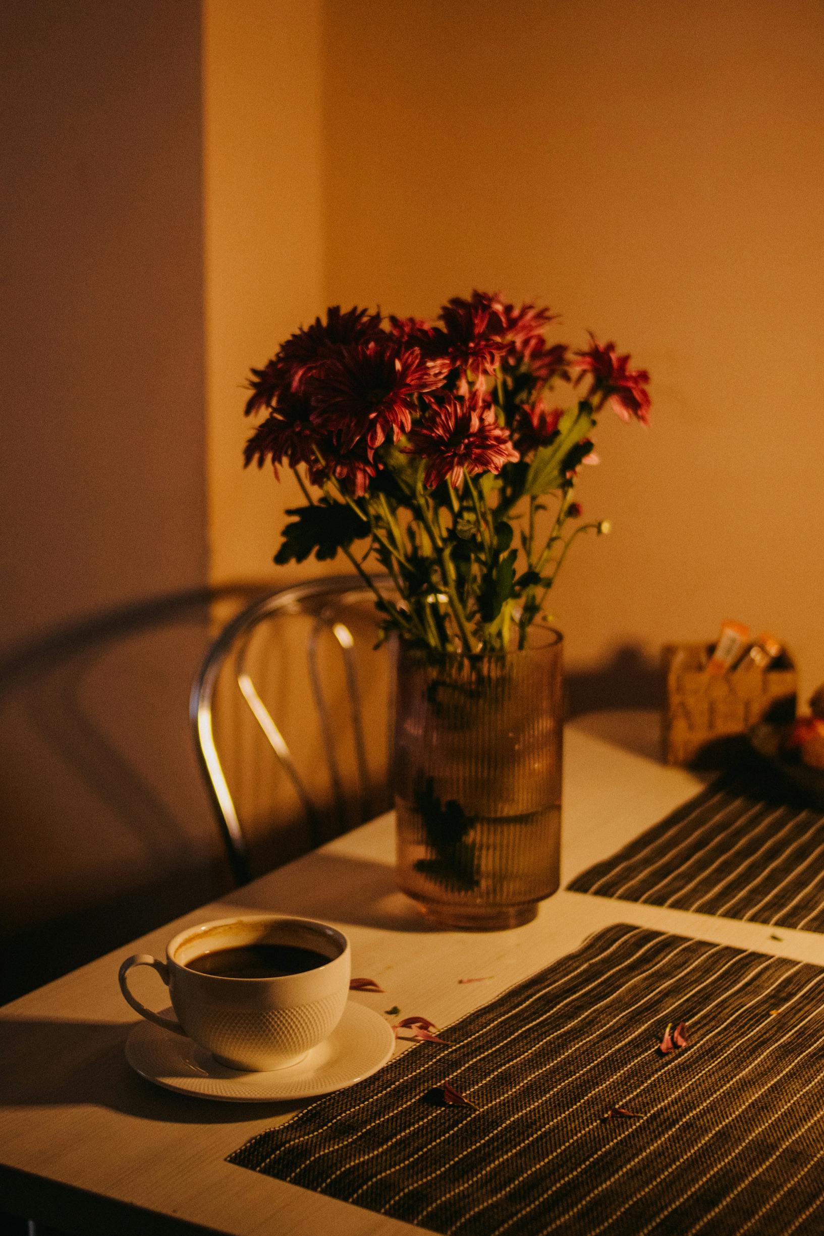 A warm, cozy scene with a coffee cup and flowers in a vase on a table at dusk.