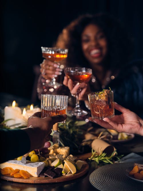 Closeup of People Making a Toast with Whiskey Glasses over a Table with Food