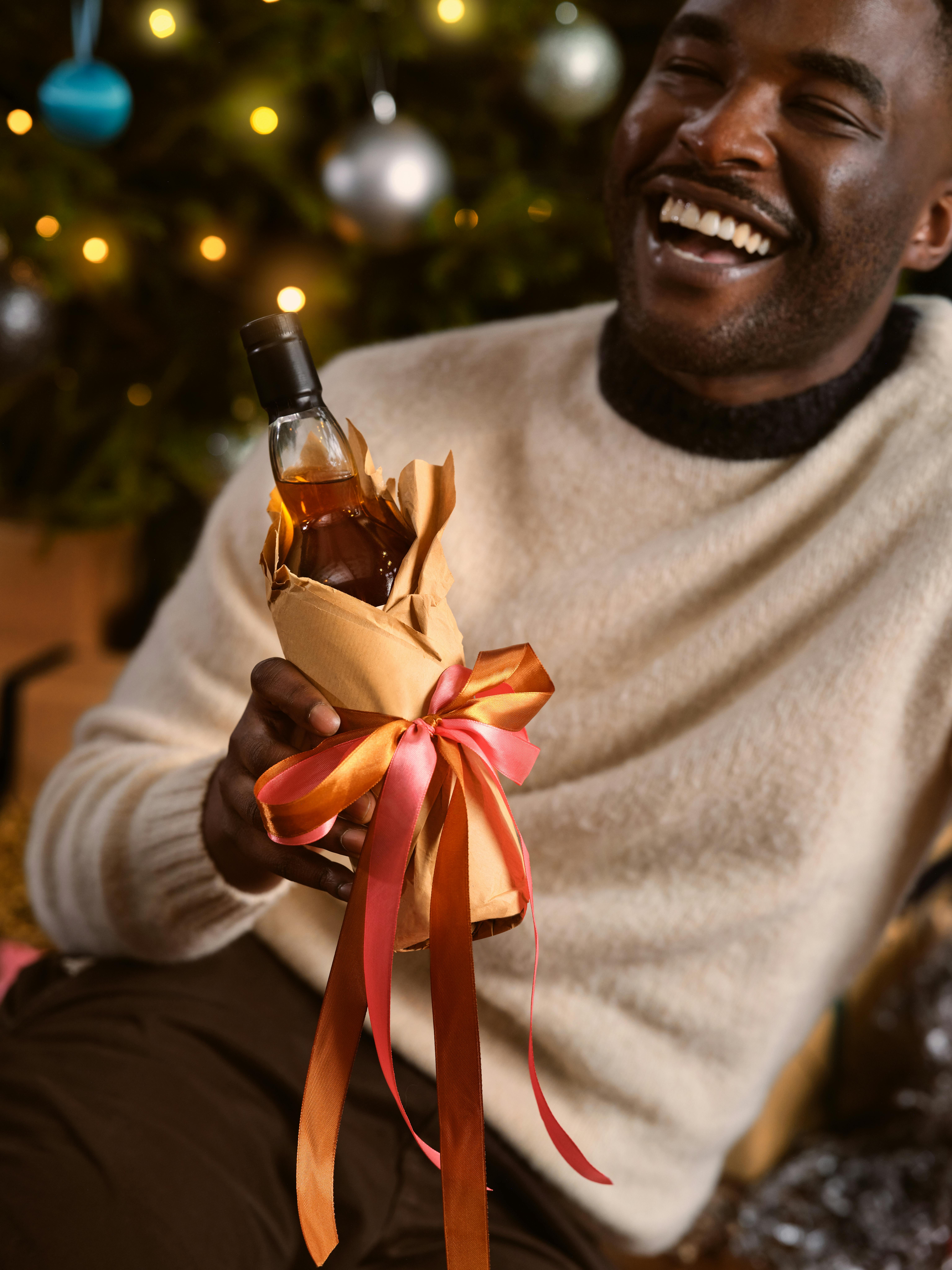 Man joyfully holding a gift-wrapped bottle in a festive Christmas setting. Perfect for holiday celebrations.