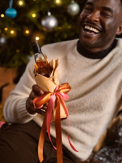 Free Man joyfully holding a gift-wrapped bottle in a festive Christmas setting. Perfect for holiday celebrations. Stock Photo