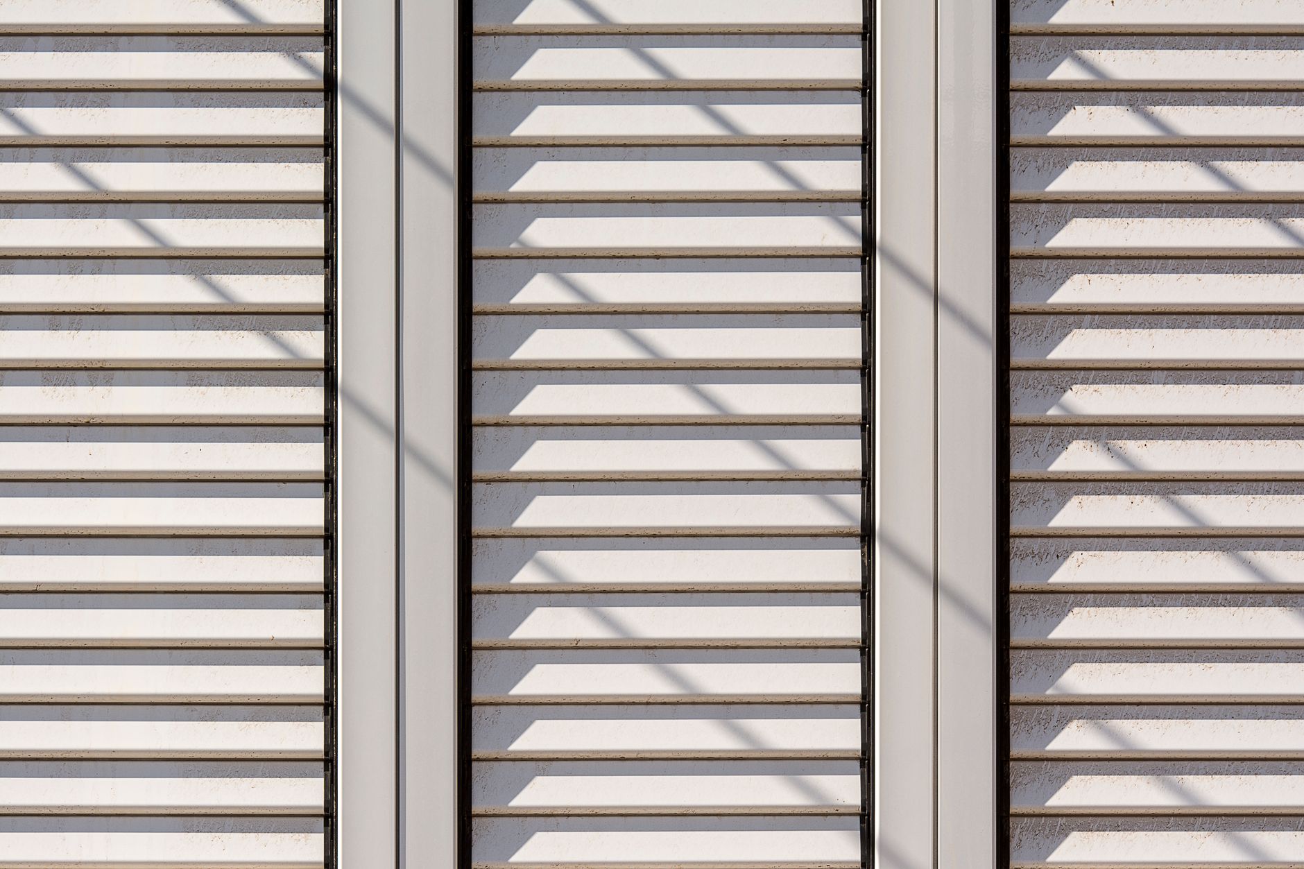 Weiße Fensterläden schützen ein Fenster vor direkter Sonne.