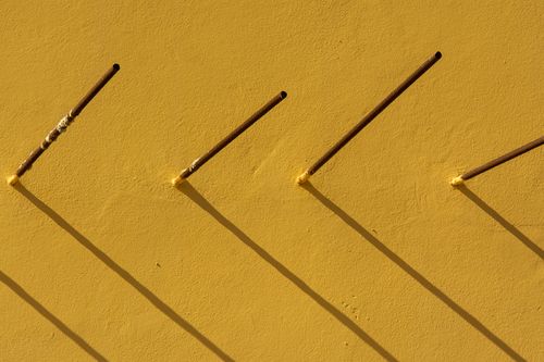 Free A minimalist photo of a yellow wall with protruding steel rods casting shadows. Stock Photo