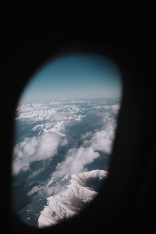 Free A breathtaking aerial view of snowy peaks from an airplane window with clouds. Stock Photo
