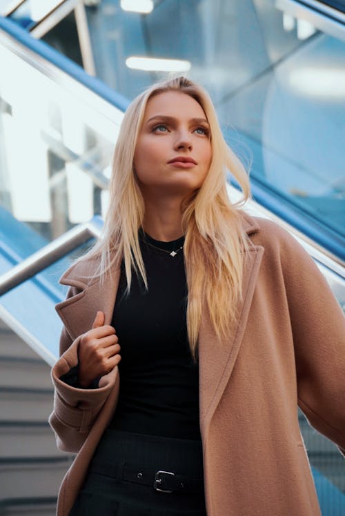 Photo of a Blonde Wearing a Beige Coat Standing on Stairs