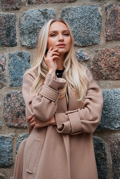 Stylish blonde woman posing against a stone wall in Berlin. Fashion and elegance captured in a vertical shot.