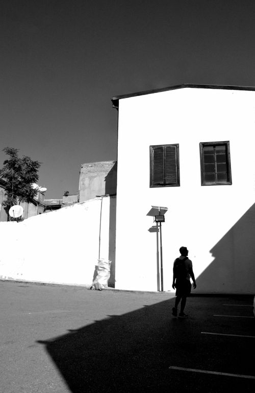Free Black and white image of a person walking past a sunlit building facade. Stock Photo