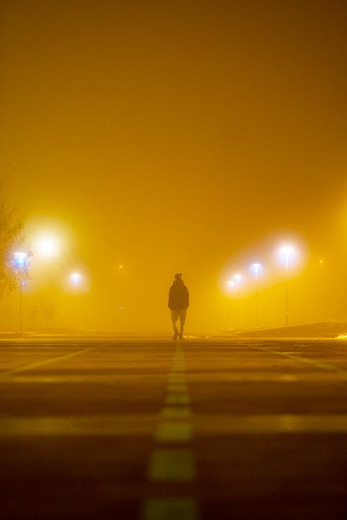 Man Walking in Solitude in Yellow Light on a Foggy Night