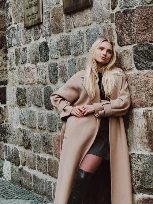 Young Woman in a Long Coat Leaning against a Stone Wall 