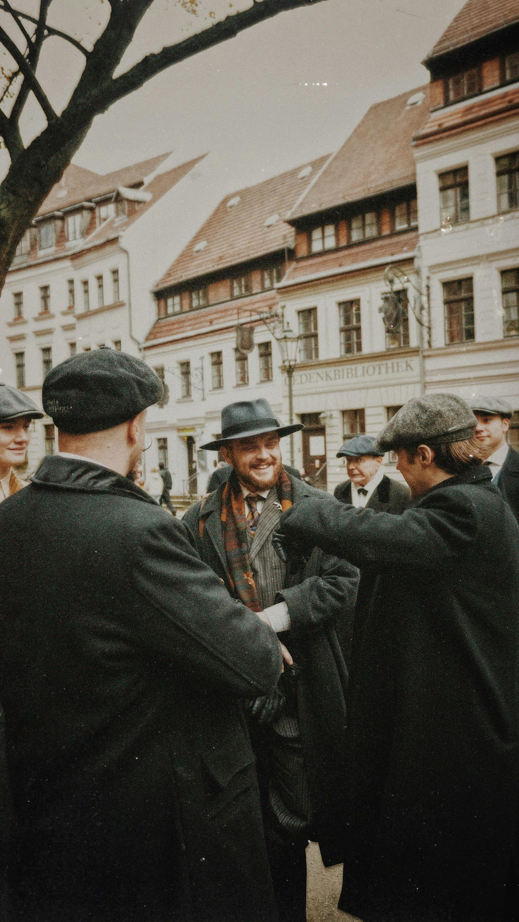A vintage-style gathering of men in coats and hats enjoying a lively conversation on a charming city street.