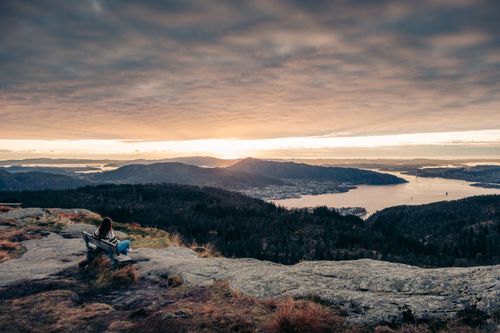 Free A woman sits on a mountain bench enjoying a stunning sunrise over Bergen, Norway. Stock Photo