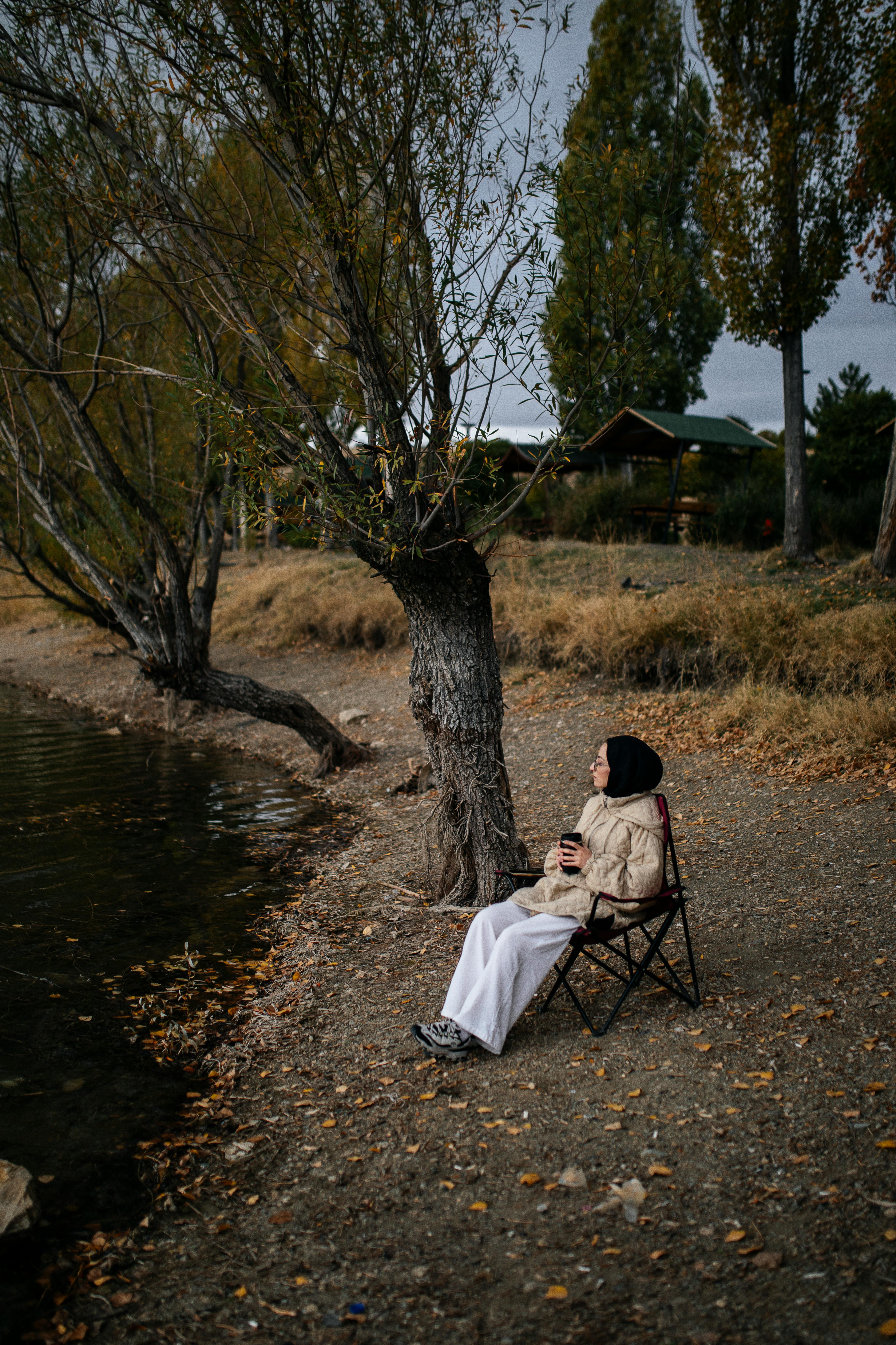 Woman relaxing by a lake in autumn, enjoying a serene moment surrounded by nature.