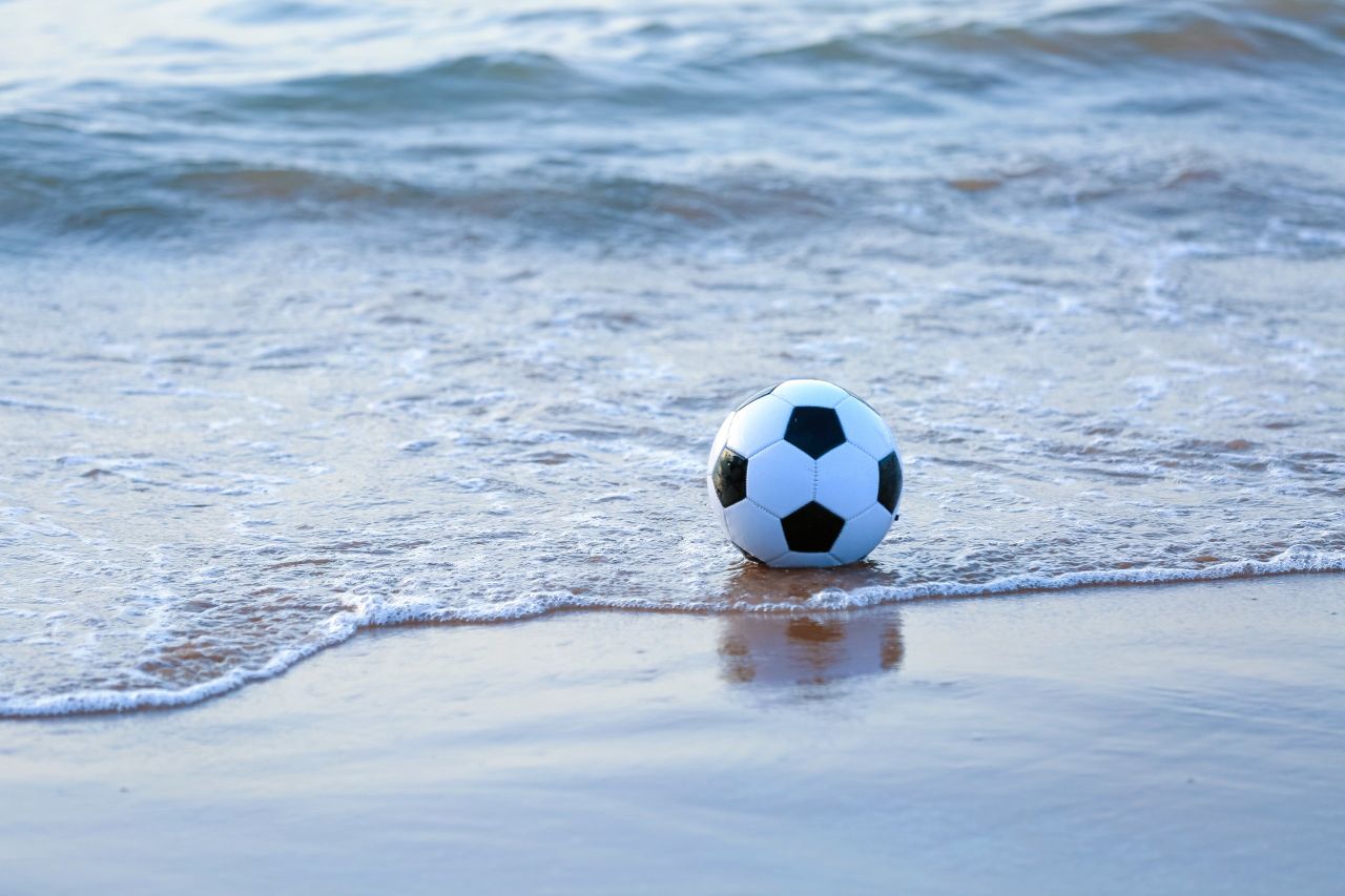 a soccer ball rests on the sandy shore as gentle waves reach it under