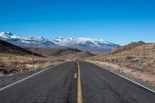 Free A picturesque road leads to snow-capped mountains under a clear blue sky, perfect for travel inspiration. Stock Photo