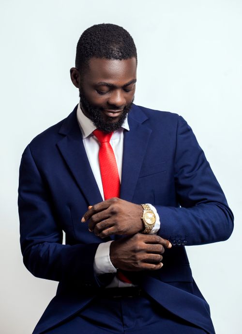 Free Elegant businessman in a navy suit adjusts his gold wristwatch, showcasing timeless fashion and professionalism. Stock Photo