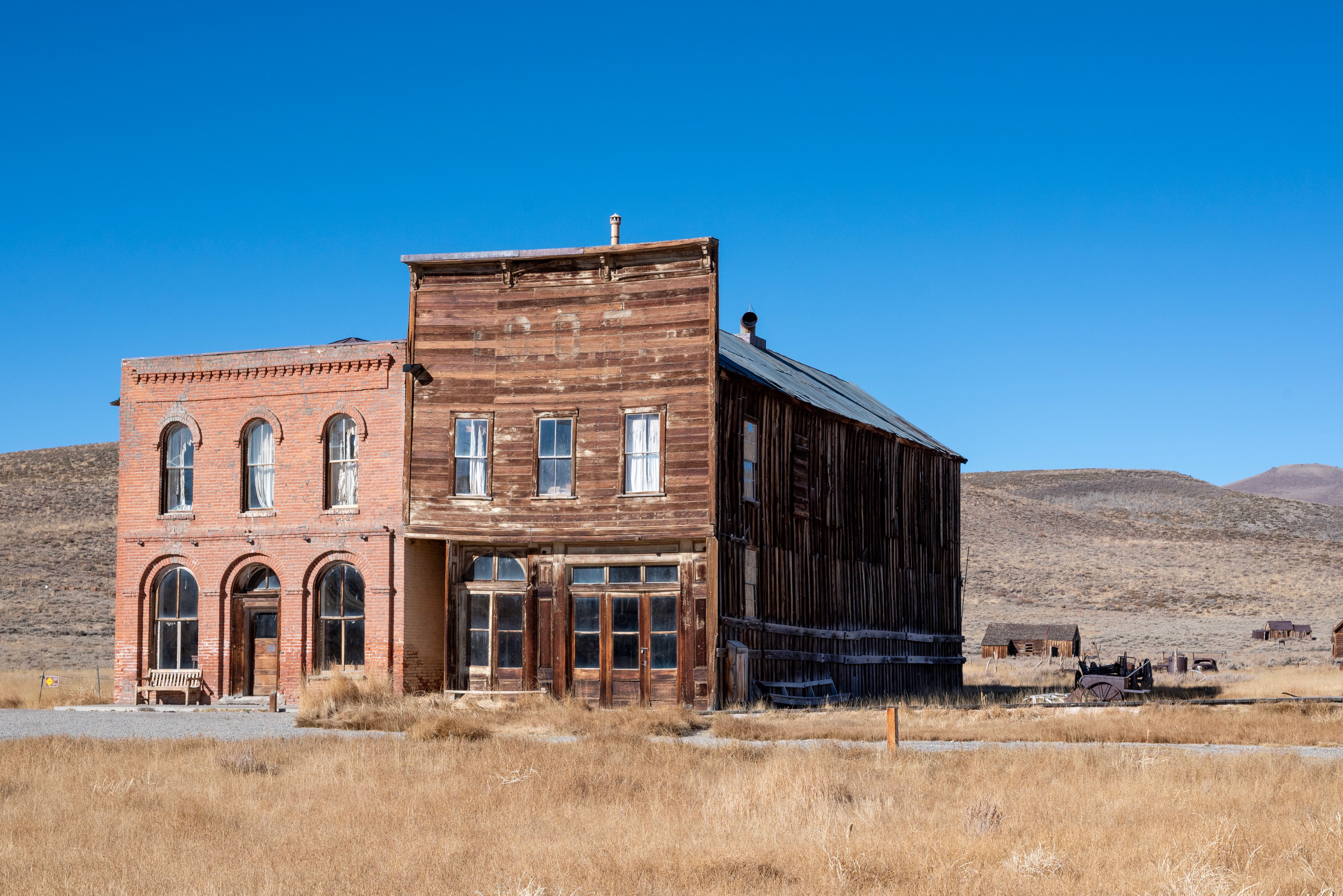 Old wooden and brick buildings in Bodie State Historic Park under a clear blue sky.