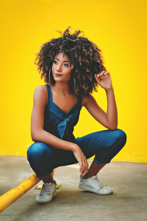 Free African American woman in blue outfit posing on a yellow background. Stock Photo