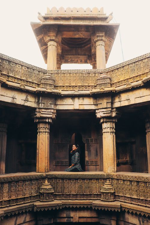 Free A woman in traditional attire poses serenely inside an ancient Indian stone temple with intricate carvings. Stock Photo