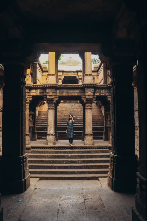 Free A woman stands in a historic Indian stepwell, showcasing intricate stone architecture. Stock Photo