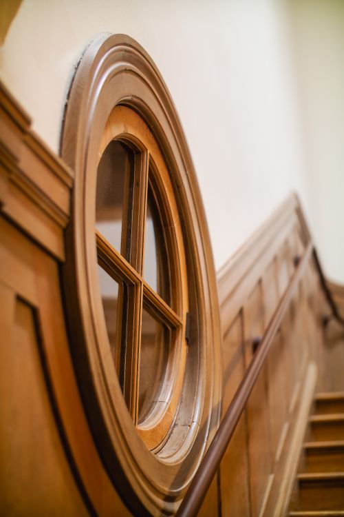 Free Circular window with wood paneling alongside an elegant wooden staircase. Stock Photo