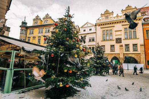 Festive Christmas market in a snow-covered Prague square with decorated trees and historic facades.