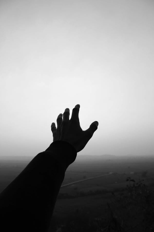 Grayscale Photo of Person's Hand Reaching For the Sky