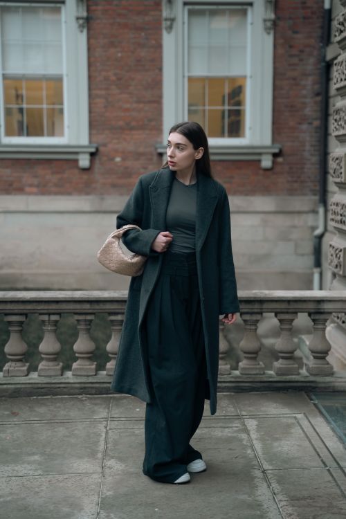 Free Fashionable woman in a long coat with wide pants standing in an urban outdoor setting. Stock Photo