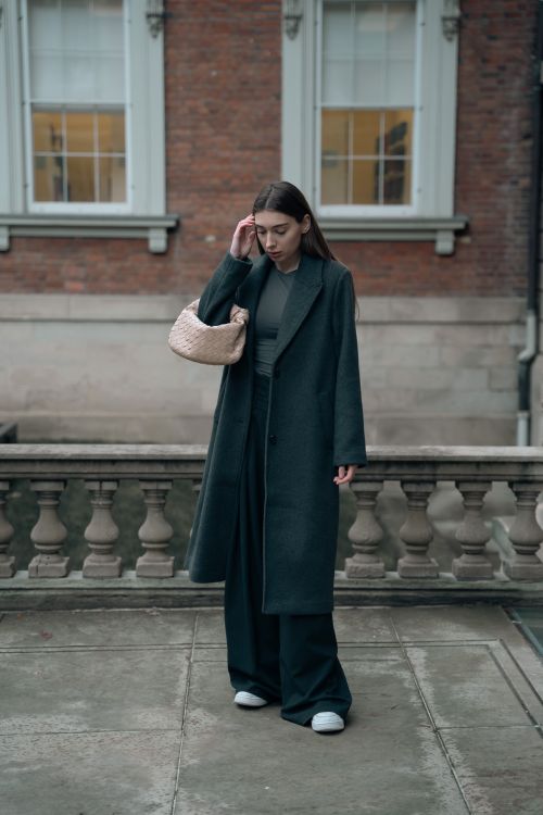 Free Fashionable woman in a gray coat and wide pants standing on a terrace with a purse. Stock Photo