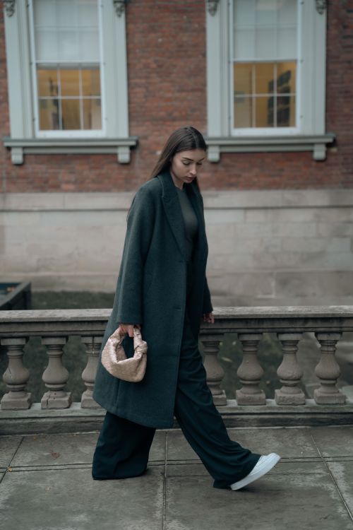 Free Stylish woman in dark coat walking along a city sidewalk, showcasing modern fashion. Stock Photo