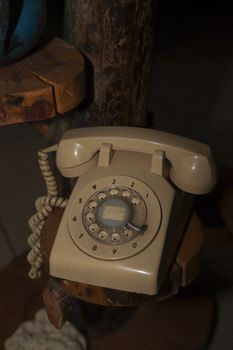 Close-up of a classic beige rotary dial telephone on a wooden shelf with ambient lighting.