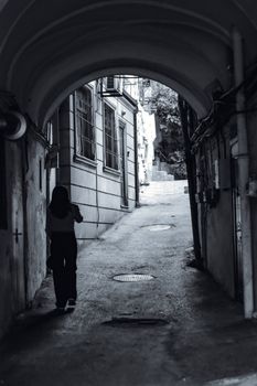 A woman walks through a narrow, arched passage in an old town.