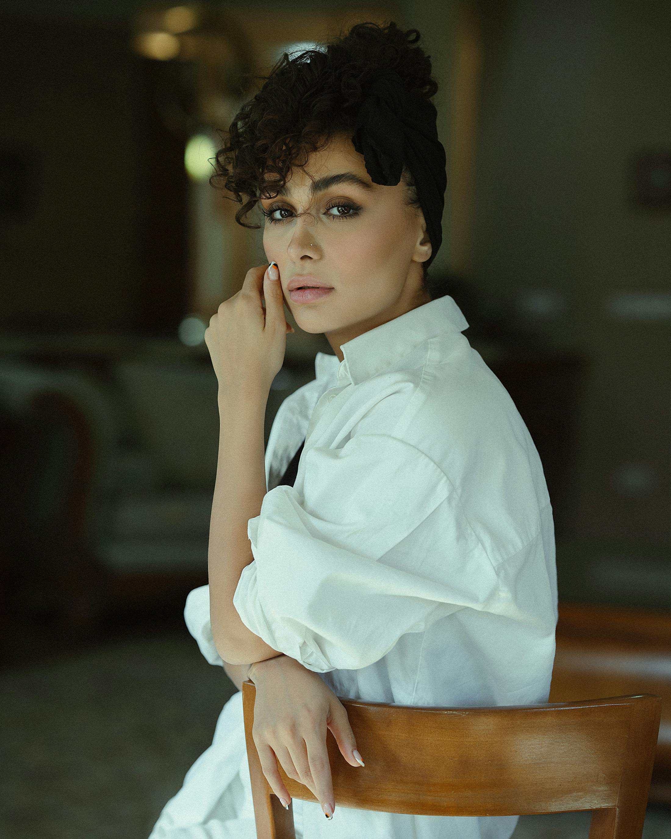 Elegant portrait of a woman sitting on a chair in a white shirt indoors.