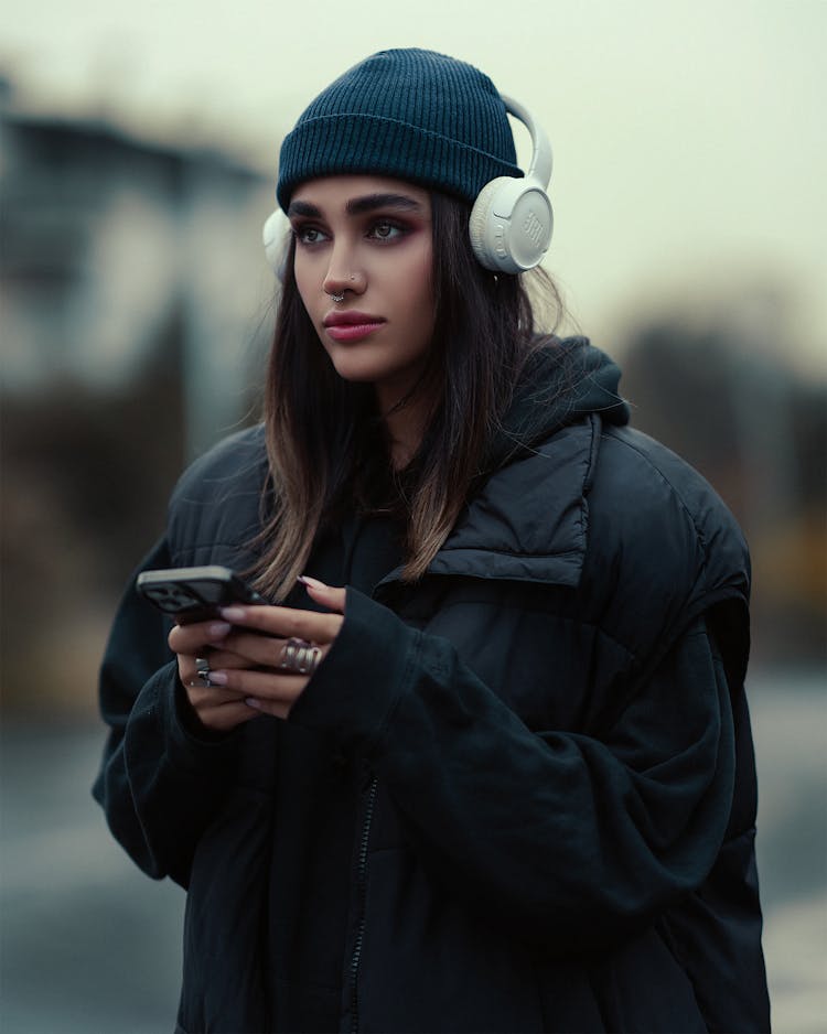 Young Fashionable Woman In A Black Outfit And Headphones Standing Outside 