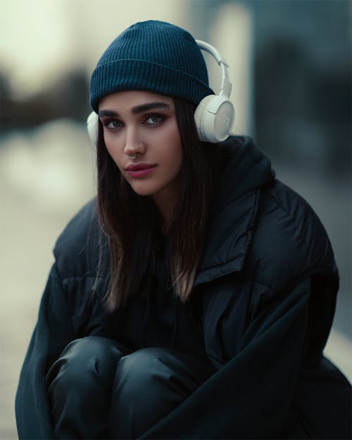 Young Fashionable Woman in a Black Outfit and Headphones Sitting Outside 