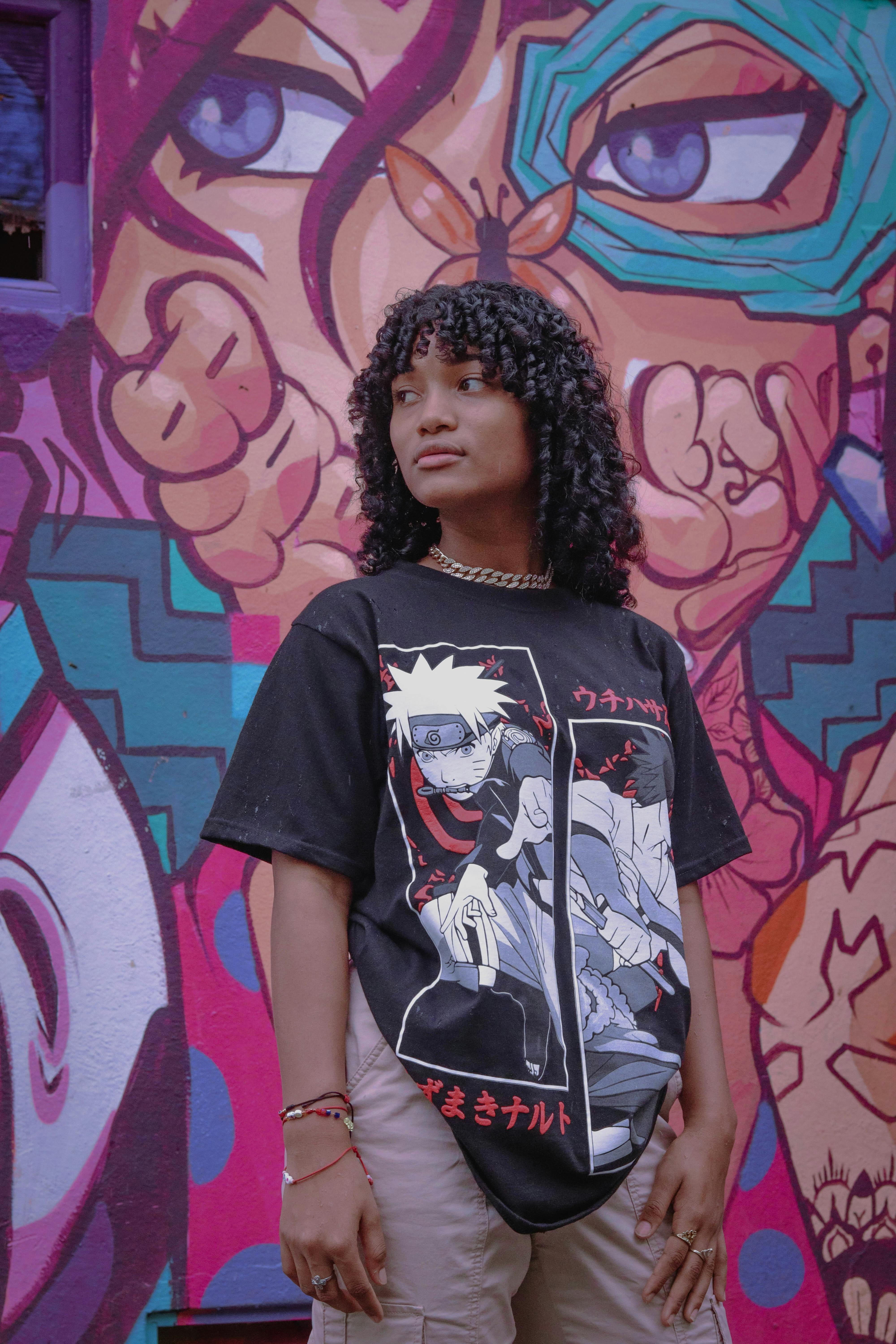 Stylish teenager with curly hair posing against a colorful mural wearing anime t-shirt.