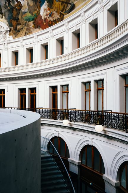 A stunning view of an elegantly curved interior featuring intricate railings and a vibrant ceiling mural.