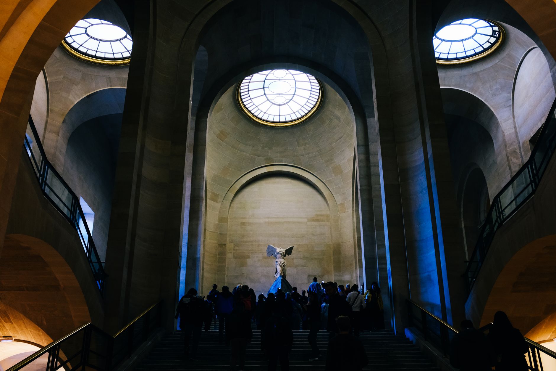 Visitors climbing the Daru staircase toward the Winged Victory of Samothrace while visiting the Louvre in Paris