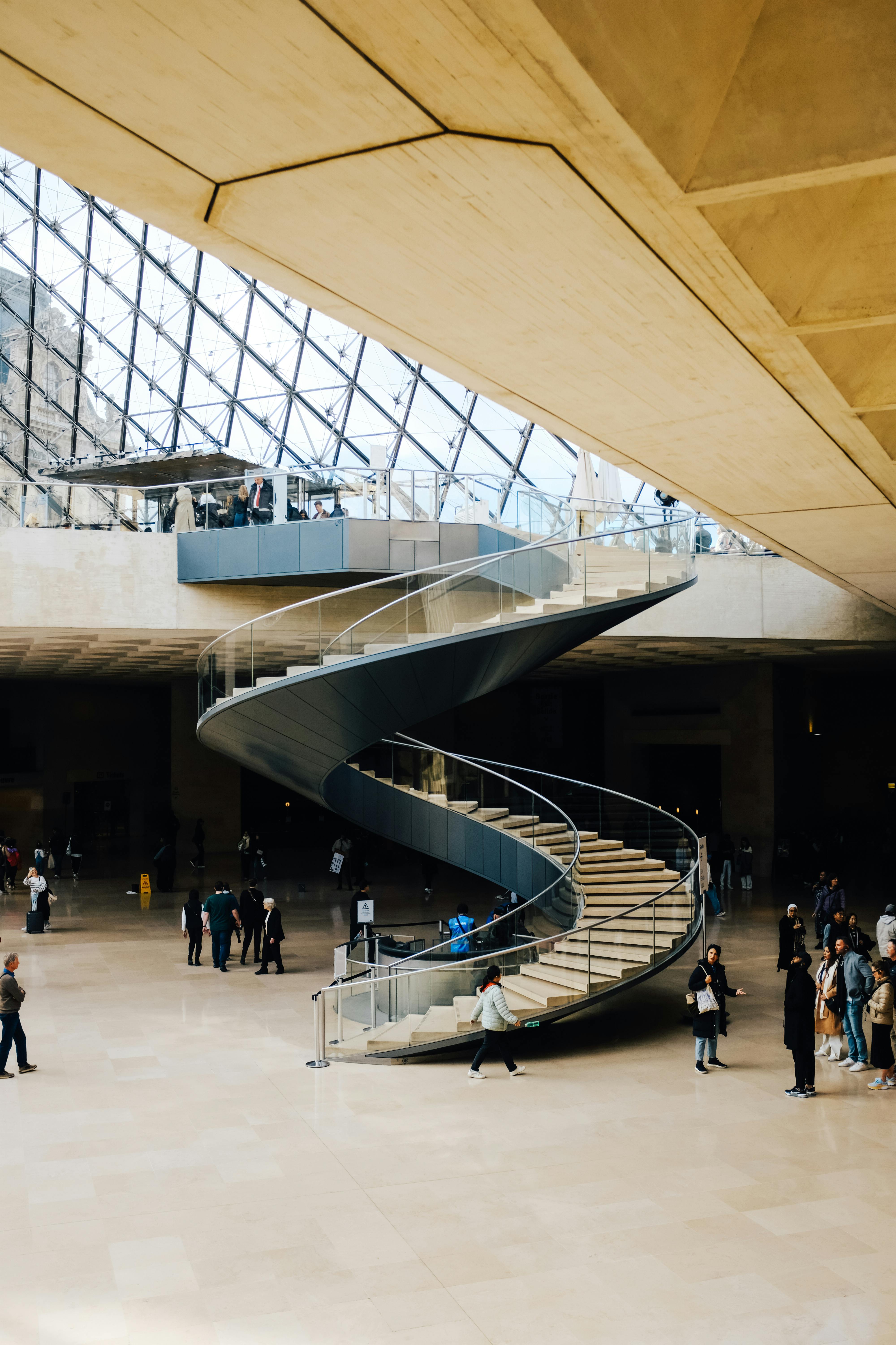Elegant spiral staircase in a bustling indoor space with modern architecture and people present.