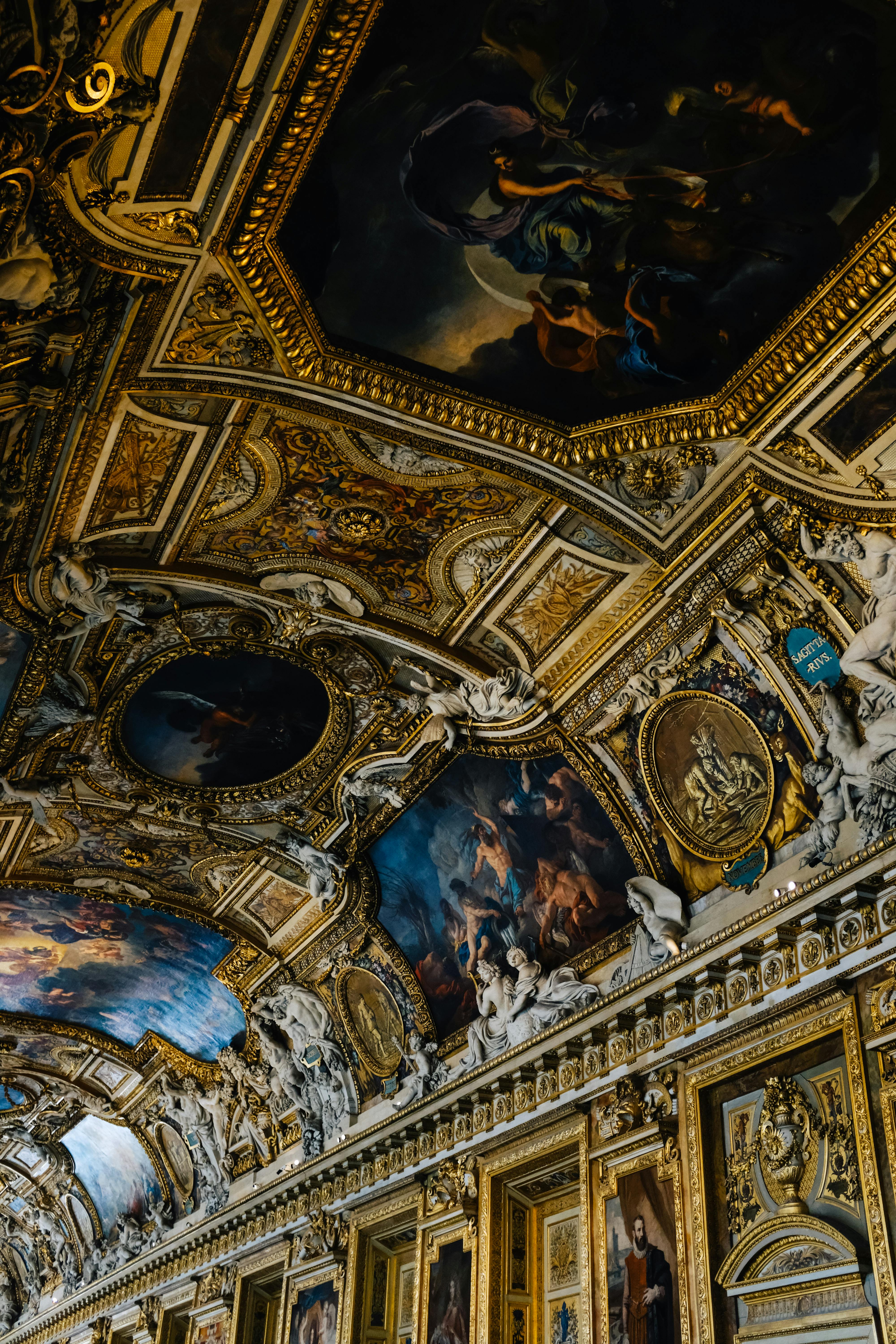 Dazzling baroque ceiling at the Louvre, featuring intricate paintings and sculptures.