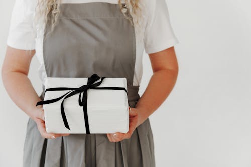 Young woman wearing apron hold in hand white present box with gift ribbon bow. Black white